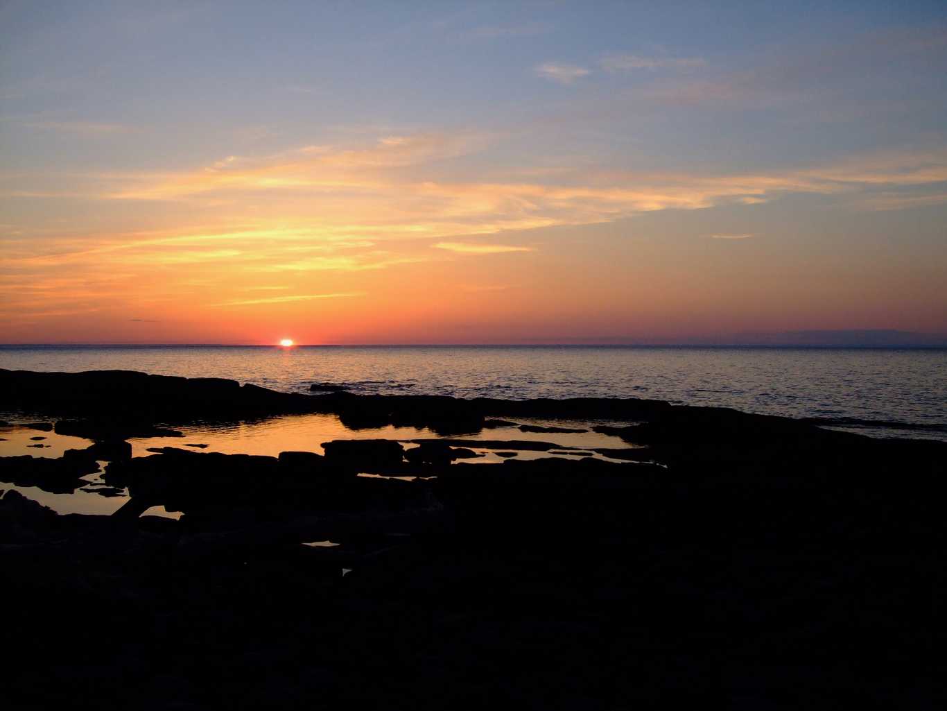 The sun sinks below the horizon over Lake Superior. In the foreground, a rocky shoreline can be barely made out. This image has nothing to do with the application, but the app contains private, proprietary data and thus a screenshot would be inappropriate.